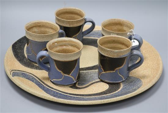 An Usch Spettigue pottery wall plaque and a set of five mugs, diameter 45.5cm